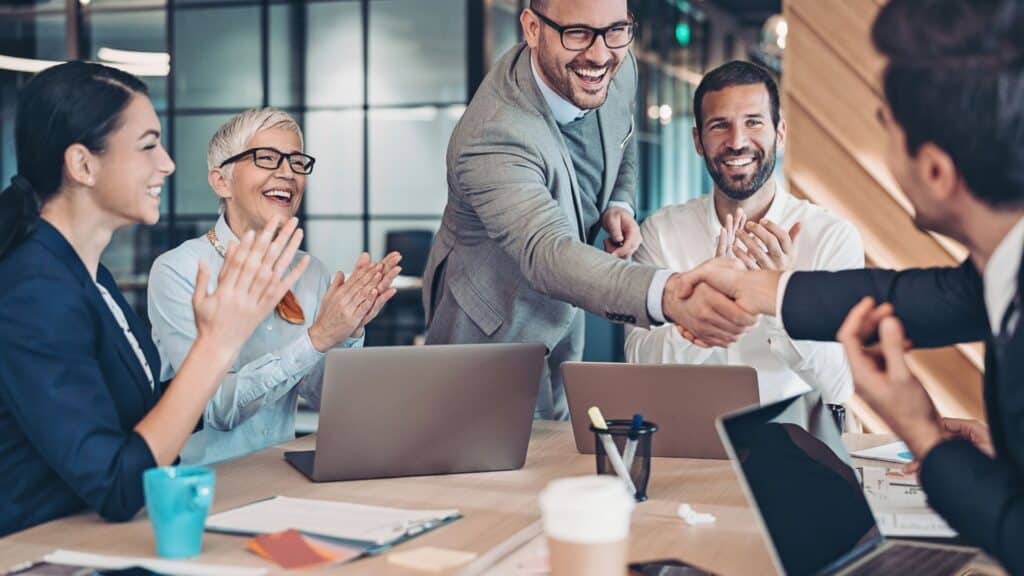 Two men giving eachother a handshake with other people clapping - B2B Matchmaking Session